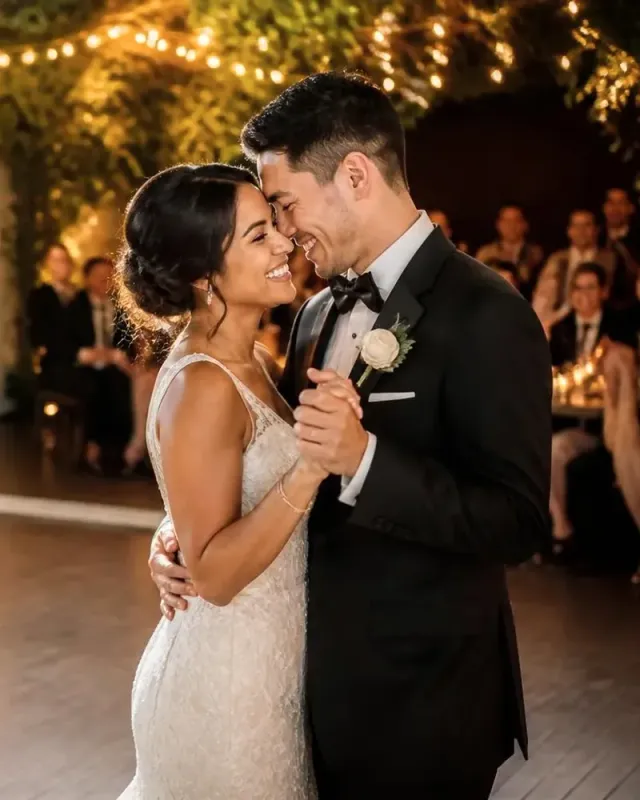A bride and groom smiling forehead to forehead during their first dance under string lights